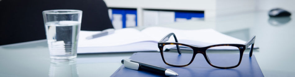 Arbeitsplatz mit Unterlagen, Brille, Stift und Glas Wasser