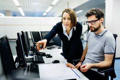 Mitarbeiterin und Mitarbeiter klären ein Problem am Arbeitsplatz umgeben von Computern