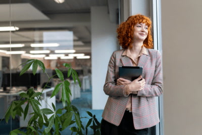 Junge Mitarbeiterin im Office blickt mit einem Lachen aus dem Fenster