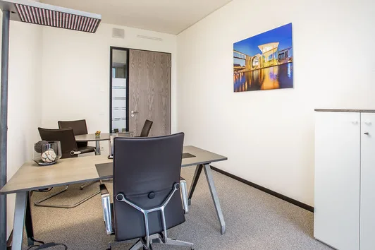 Moderner Büroraum mit mehreren Schreibtischen, ergonomischen schwarzen Bürostühlen, einem farbigen Wandbild und einem weißen Schrank.