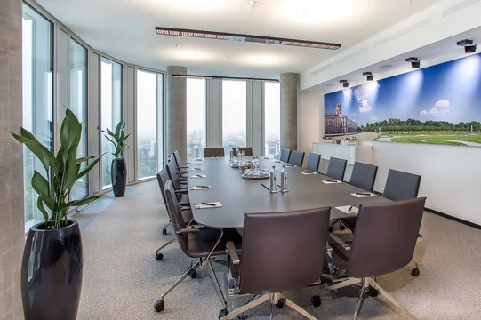 Moderner Konferenzraum mit großem ovalen Tisch, vielen Bürostühlen, raumhohen Fenstern mit Stadtblick und Wandbild.
