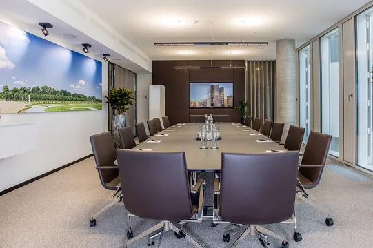 Moderner Konferenzraum mit langem Tisch, vielen Stühlen, großem Bildschirm und einer Wand mit Landschaftsfototapete.