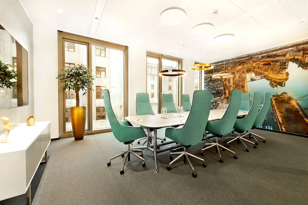 Moderner Konferenzraum mit langem weißen Tisch, türkisfarbenen Bürostühlen, großen Fenstern und einer Stadtwandtapete.