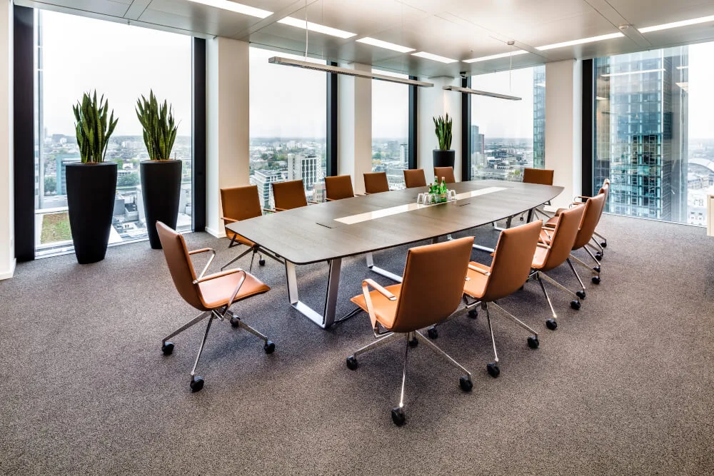 Modern eingerichteter Konferenzraum mit langem Holztisch, braunen Lederstühlen, großen Fenstern und weitem Stadtblick.