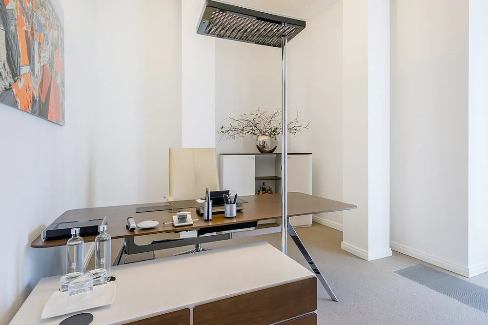 Modernes, helles Bürozimmer mit großem Holzschreibtisch, beigem Chefsessel, Stehlampe und Wandkunst.