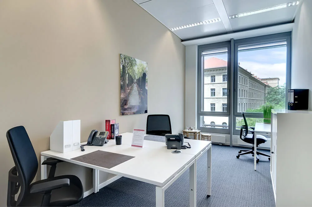 Helles, modernes Bürozimmer mit zwei weißen Schreibtischen, zwei Bürostühlen, Telefonen und einem großen Fenster mit Stadtblick.