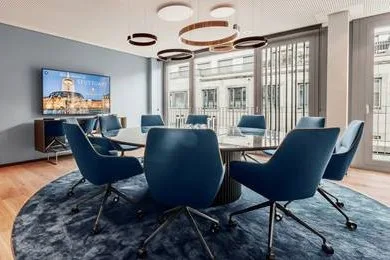 Moderner Konferenzraum mit großem runden Tisch, blauen Stühlen, großem TV-Bildschirm mit Stuttgart-Panorama und Fenstern.