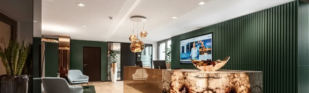 Moderne Lobby mit grüner Lamellenwand, leuchtender Rezeptionstheke aus Onyx, großem Bildschirm, goldenen Pendelleuchten und Sitzgelegenheiten.